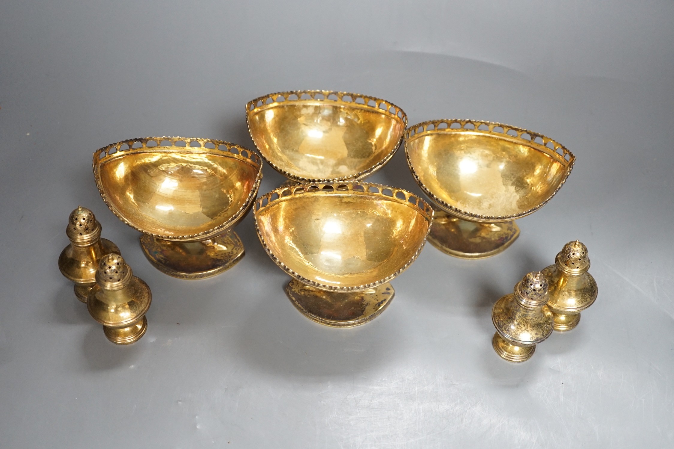 A set of four 20th century Spanish gilt white metal boat shaped pedestal bowls, with pierced borders, on twin dolphin supports 10.3cm and a set of four similar pepperettes, 18oz.